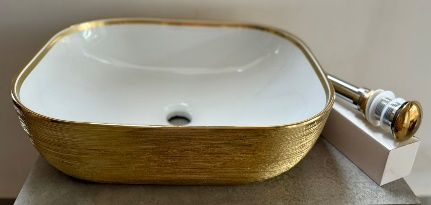Fregadero de cerámica blanca con exterior texturizado dorado. Tiene borde y tapón de desagüe dorados.