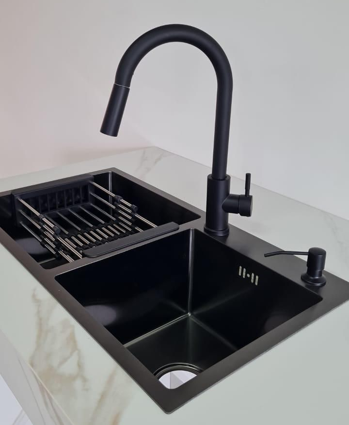Fregadero de cocina negro con grifo negro y escurridor de platos incorporado sobre una encimera blanca.