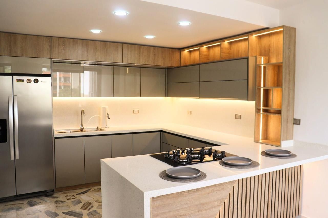 Cocina moderna con gabinetes de madera clara y gris, electrodomésticos de acero inoxidable y una isla de encimera blanca.