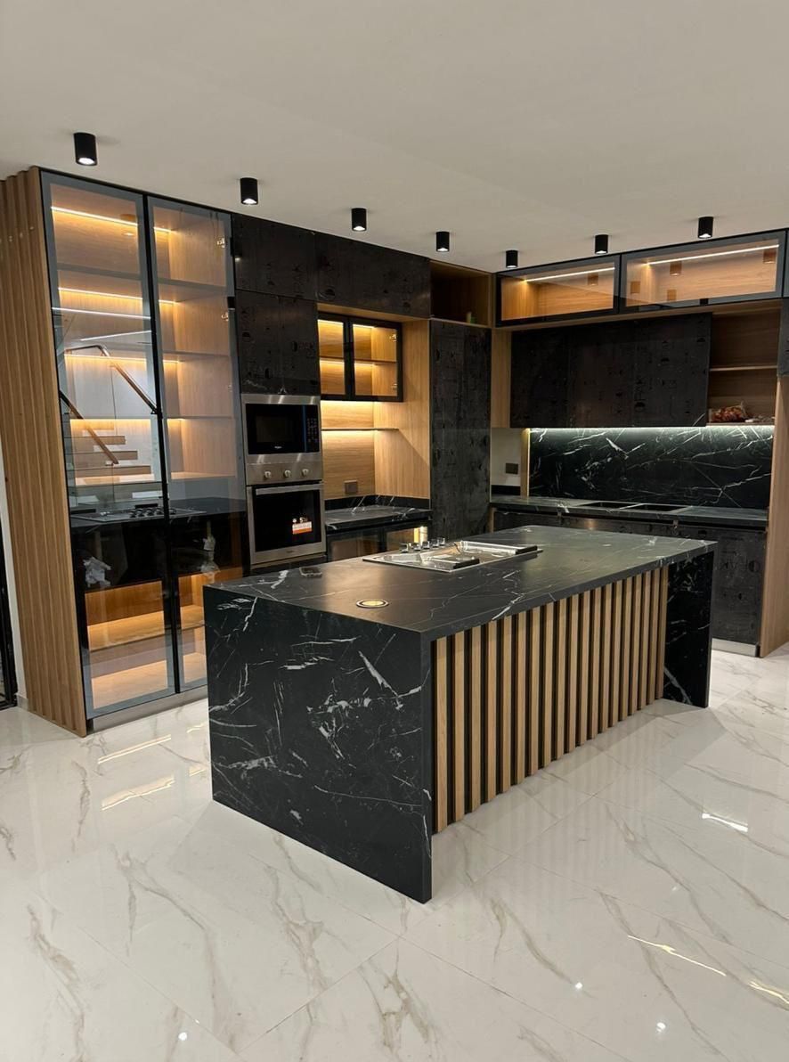 Cocina moderna con isla de mármol negro, gabinetes oscuros y detalles de madera.