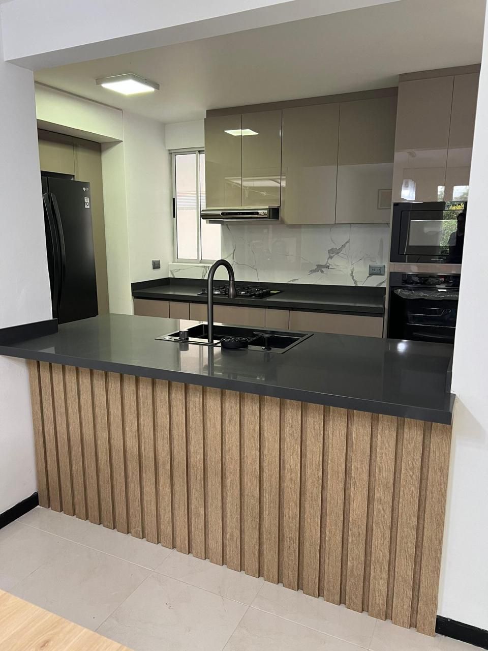 Cocina moderna con encimera negra y gabinetes beige, con una isla de listones de madera clara.