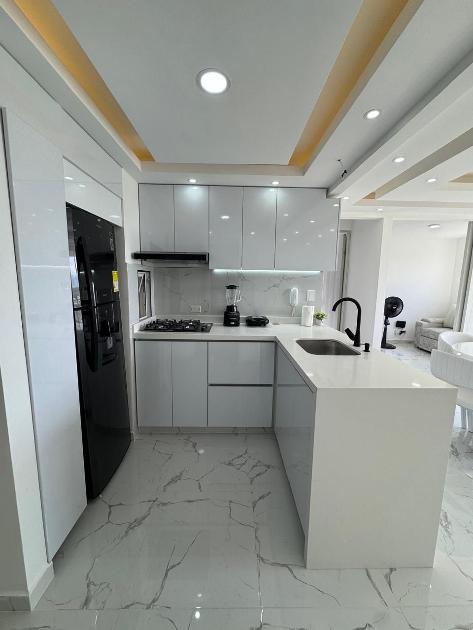 Cocina blanca moderna con refrigerador, encimeras y electrodomésticos negros.