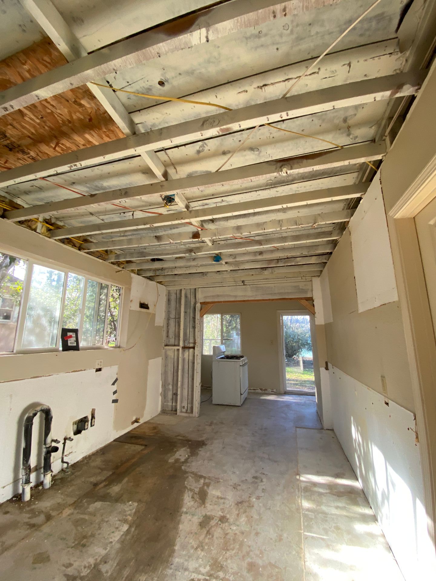 Renovated room with exposed ceiling beams, unfinished walls, concrete floor, and a bright doorway at the far end