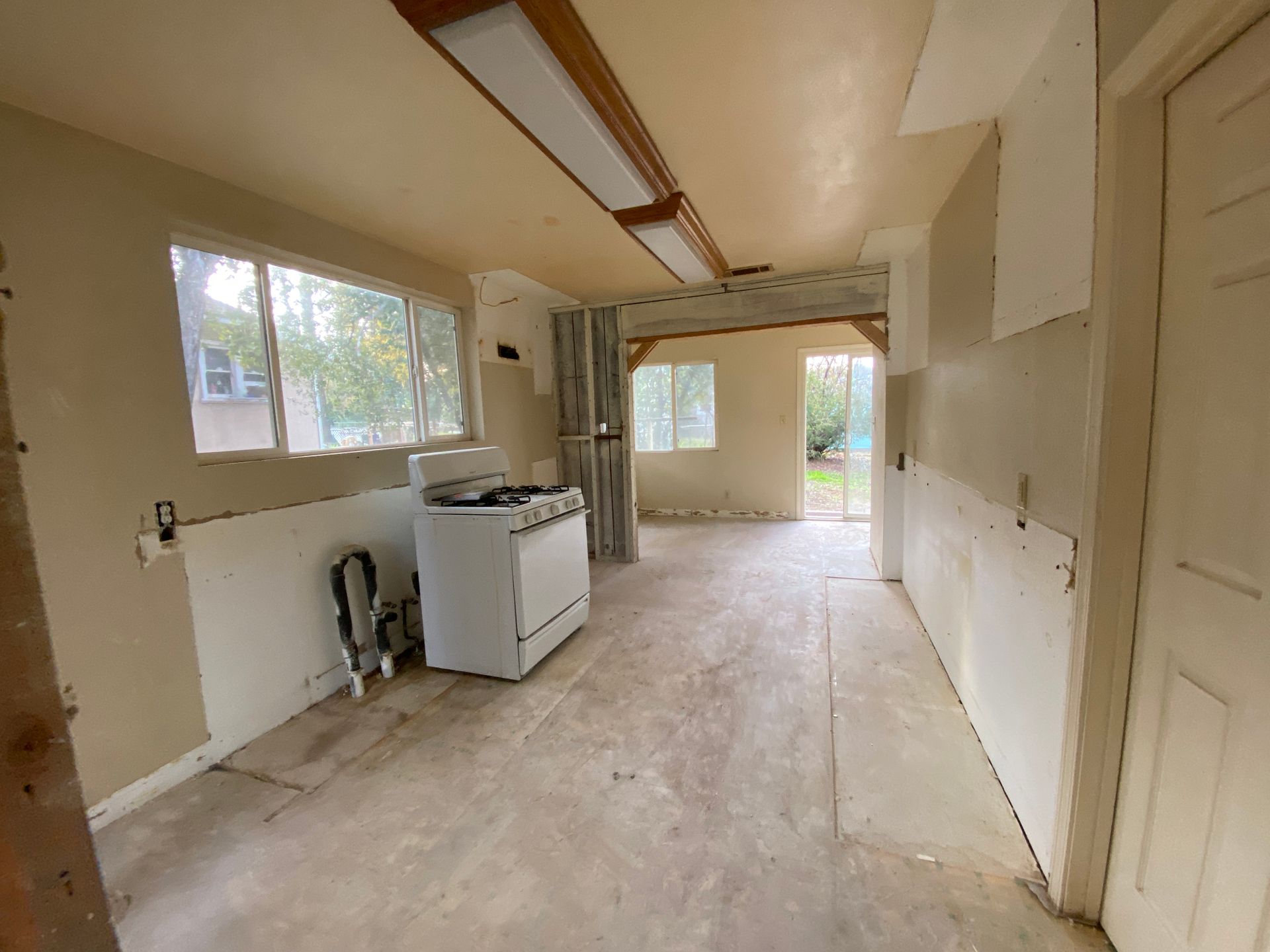 Empty unfinished kitchen with exposed walls, white stove, windows, and a view into another room