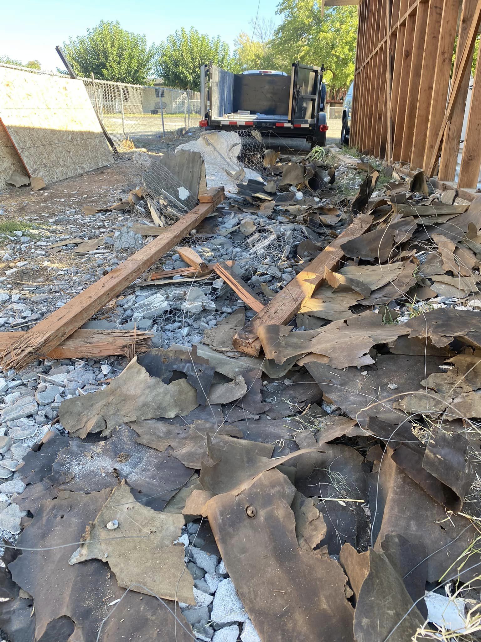 Burned debris and charred roofing scattered along a narrow alley beside a truck and wooden fence