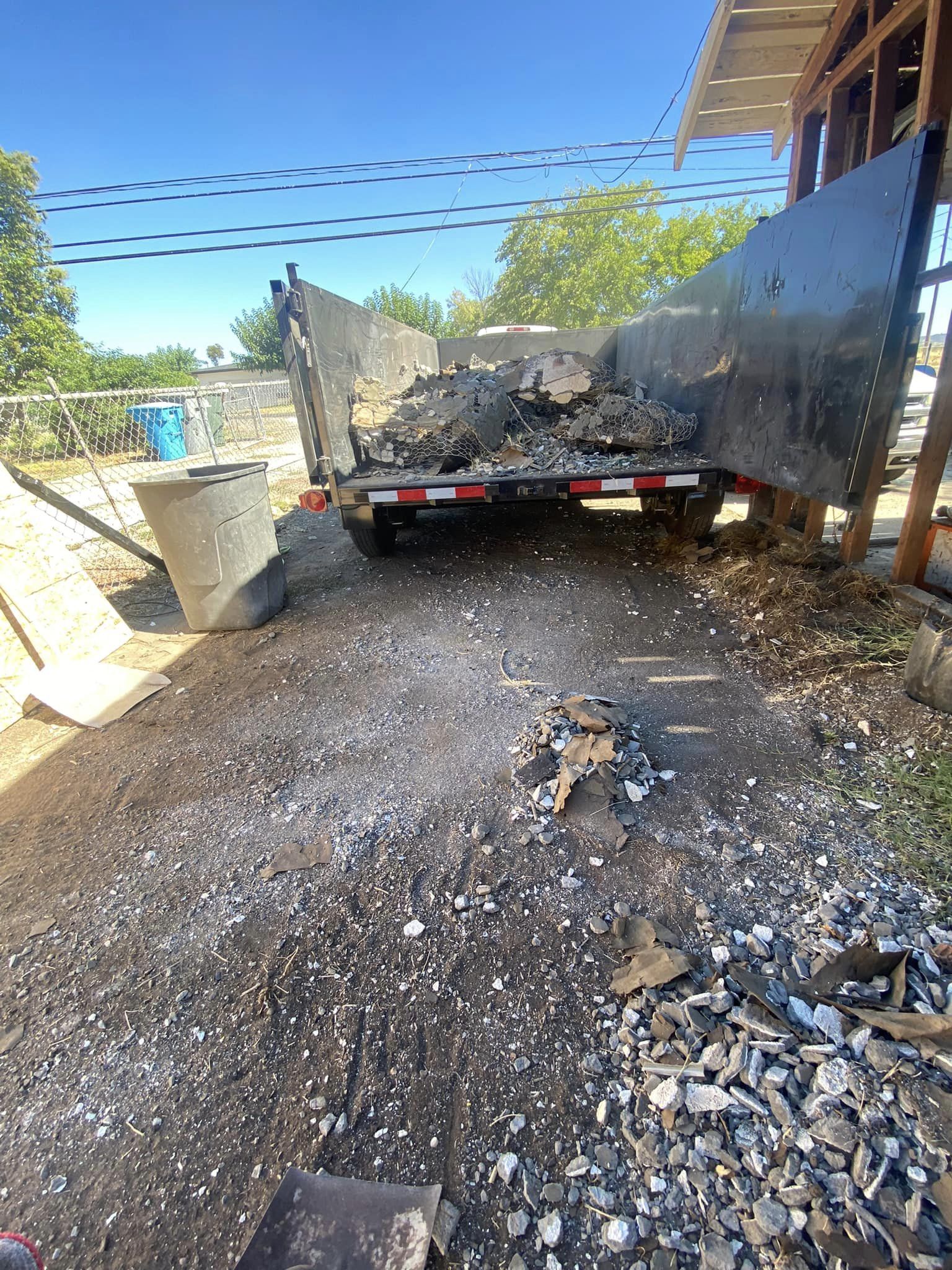 Dump truck backing into a gravel pile beside a building on a sunny work site