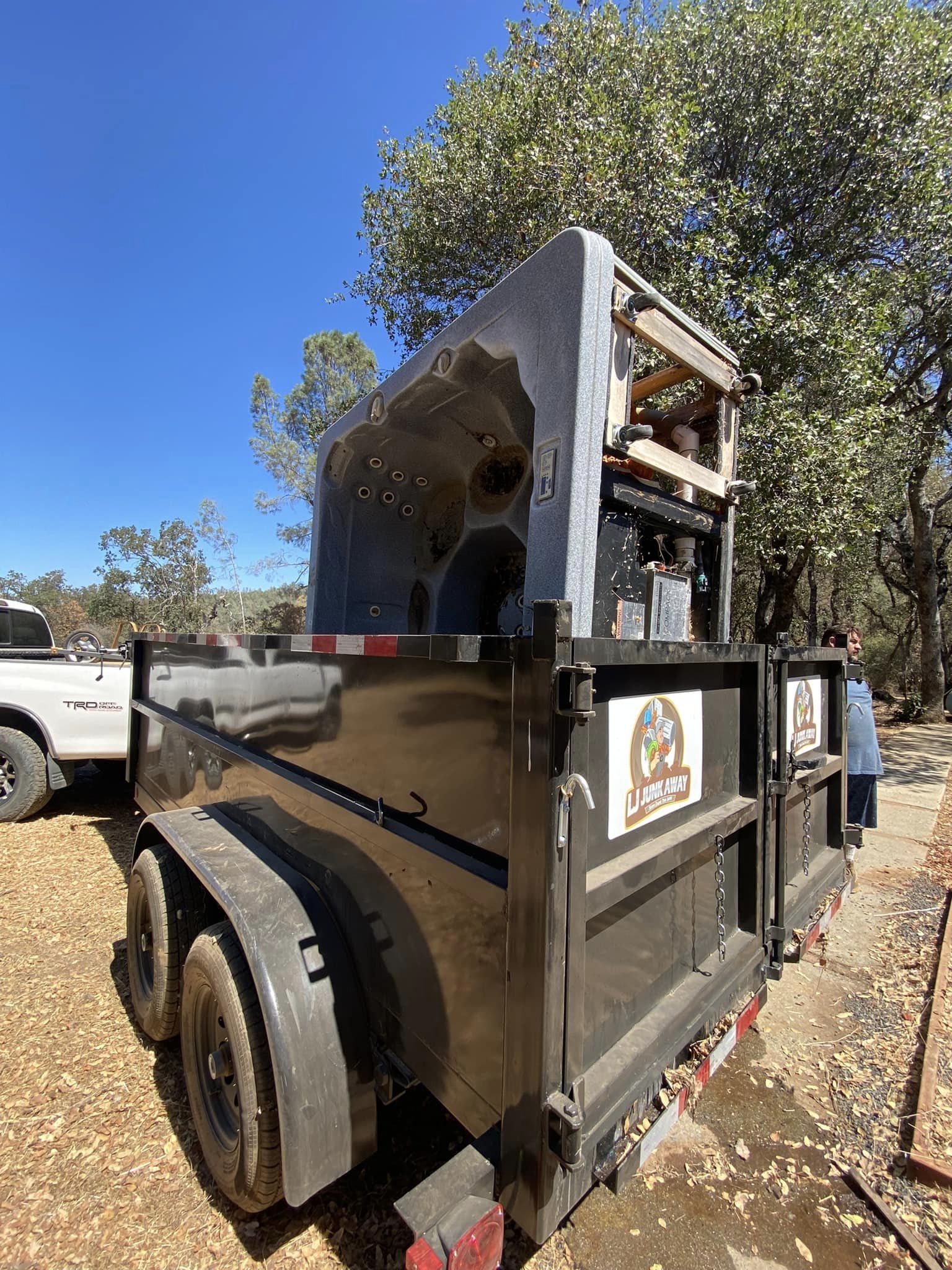 Black trailer-mounted outdoor grill smoker parked beside a white truck under trees.