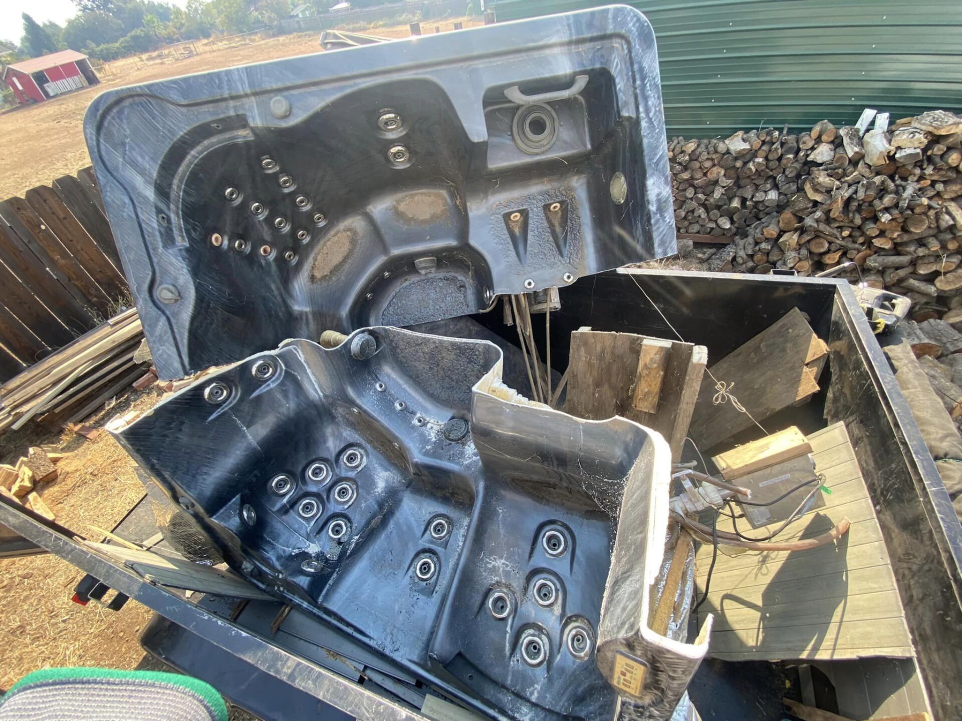 Damaged black hot tub shell with broken wooden frame, sitting outdoors on debris.