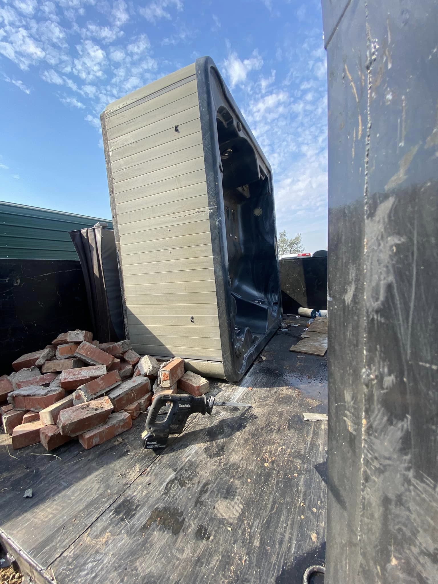 Charred shipping container tipped over beside a pile of bricks under a blue sky