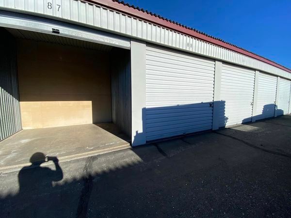 Open storage unit with white roll-up door, metal siding, and shadow on the asphalt driveway.