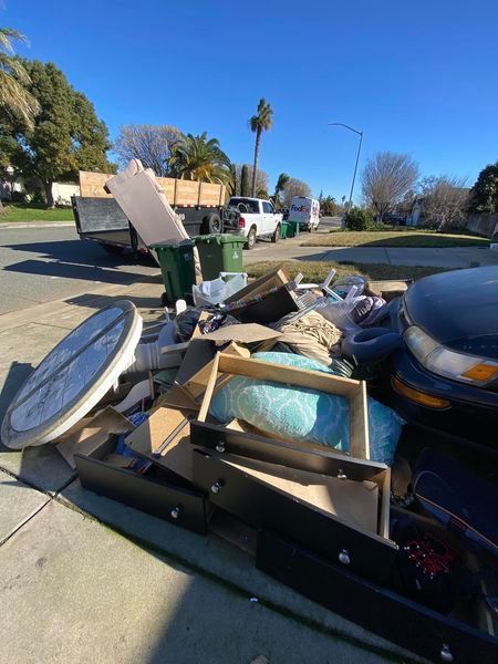 Overflowing curbside junk pile with furniture and household debris on a sunny street corner