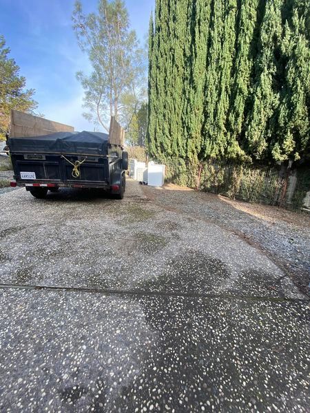 Black SUV parked on a gravel driveway beside tall hedges and trees on a sunny day