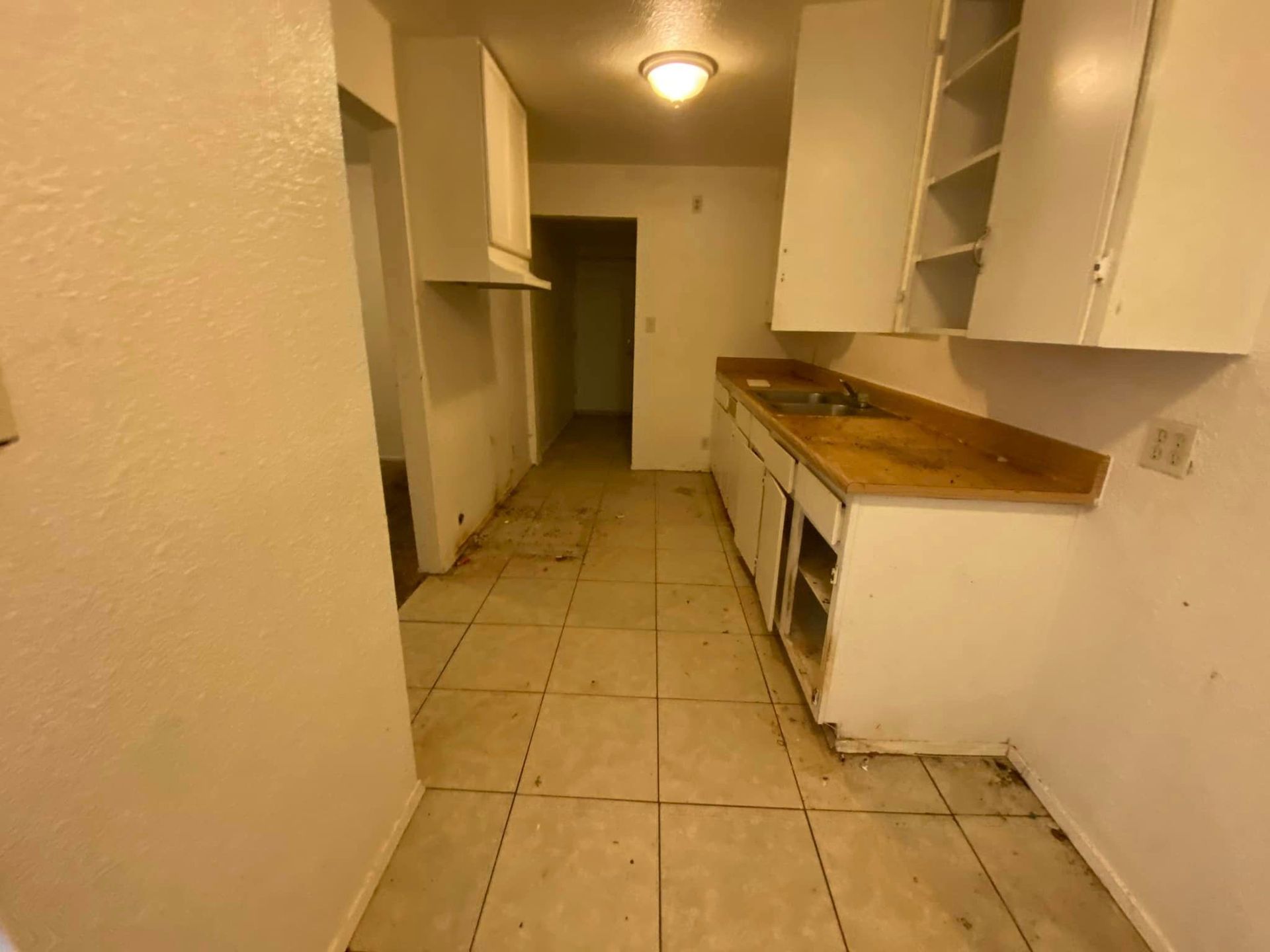Narrow empty kitchen with white cabinets, brown countertop, and tiled floor.