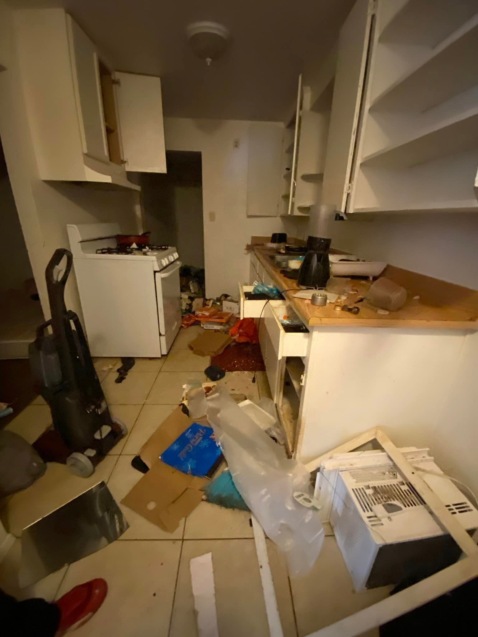 Cluttered narrow kitchen with boxes, scattered items, and a messy countertop near a white refrigerator.