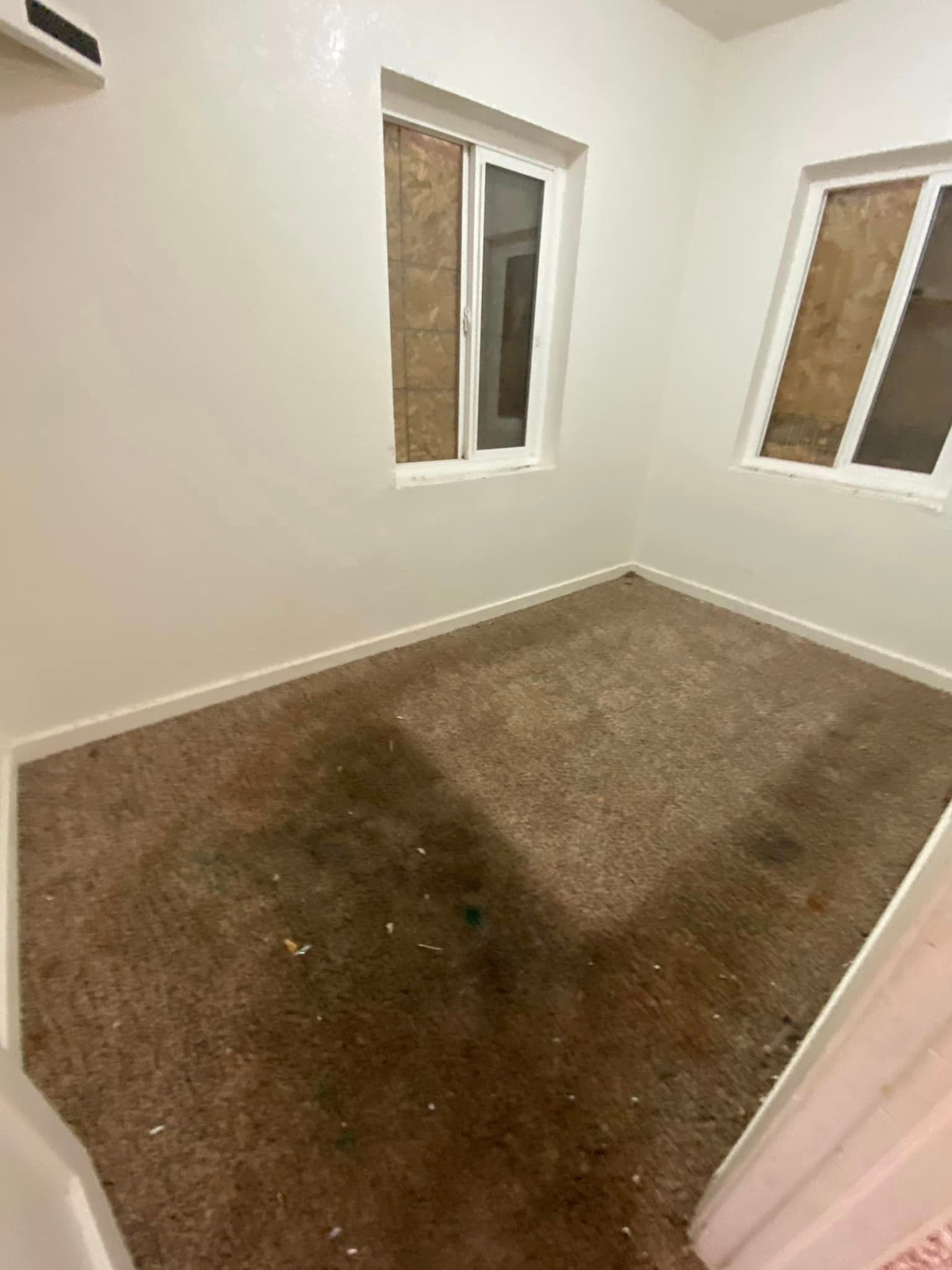 Empty white room with two windows and a large brown stain on the carpet.
