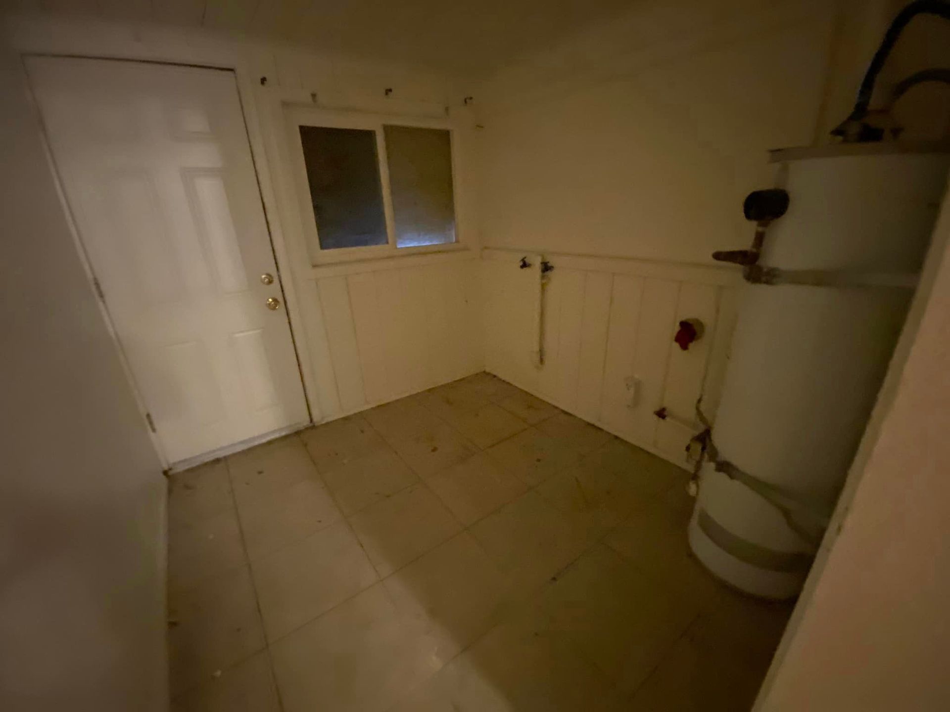Small tiled utility room with a door, window, wall pipes, and a large water heater.