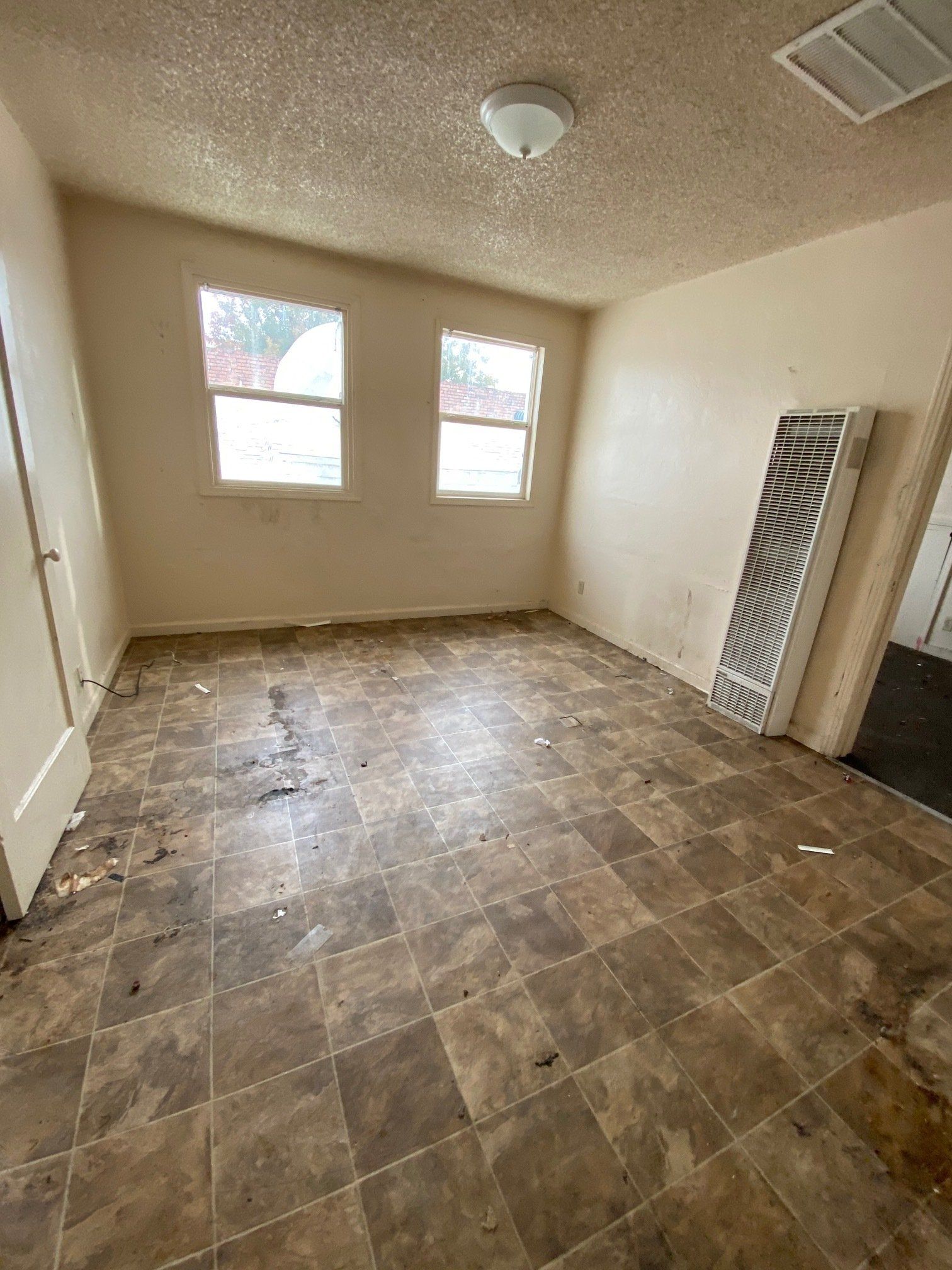 Empty beige room with two windows, brown tile floor, ceiling fan, and a wall-mounted vent unit