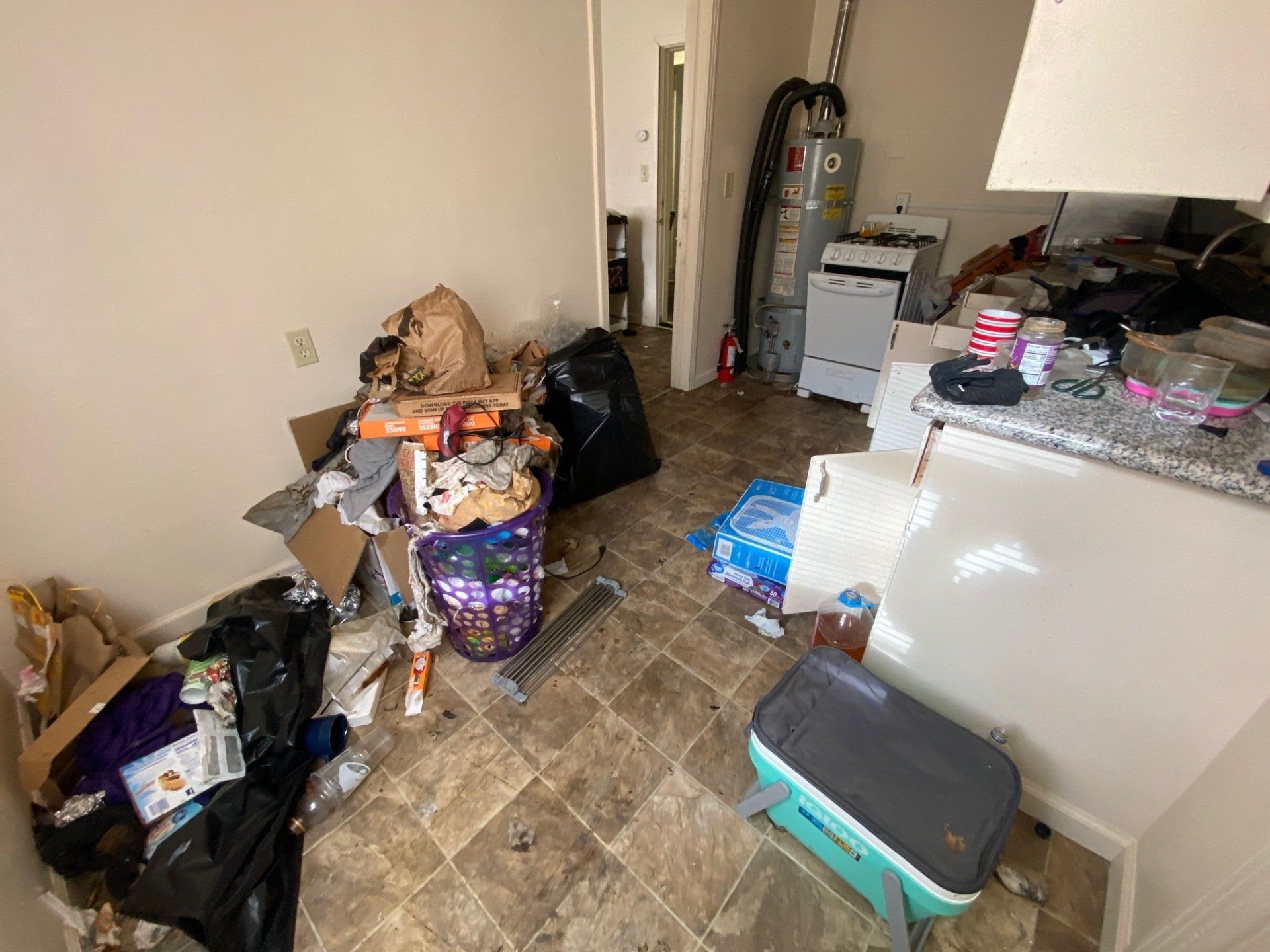 Cluttered kitchen with trash bags, boxes, and scattered items on the floor and counters