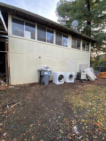 Exterior of beige house with trash bins, two air conditioners, and a satellite dish along the wall
