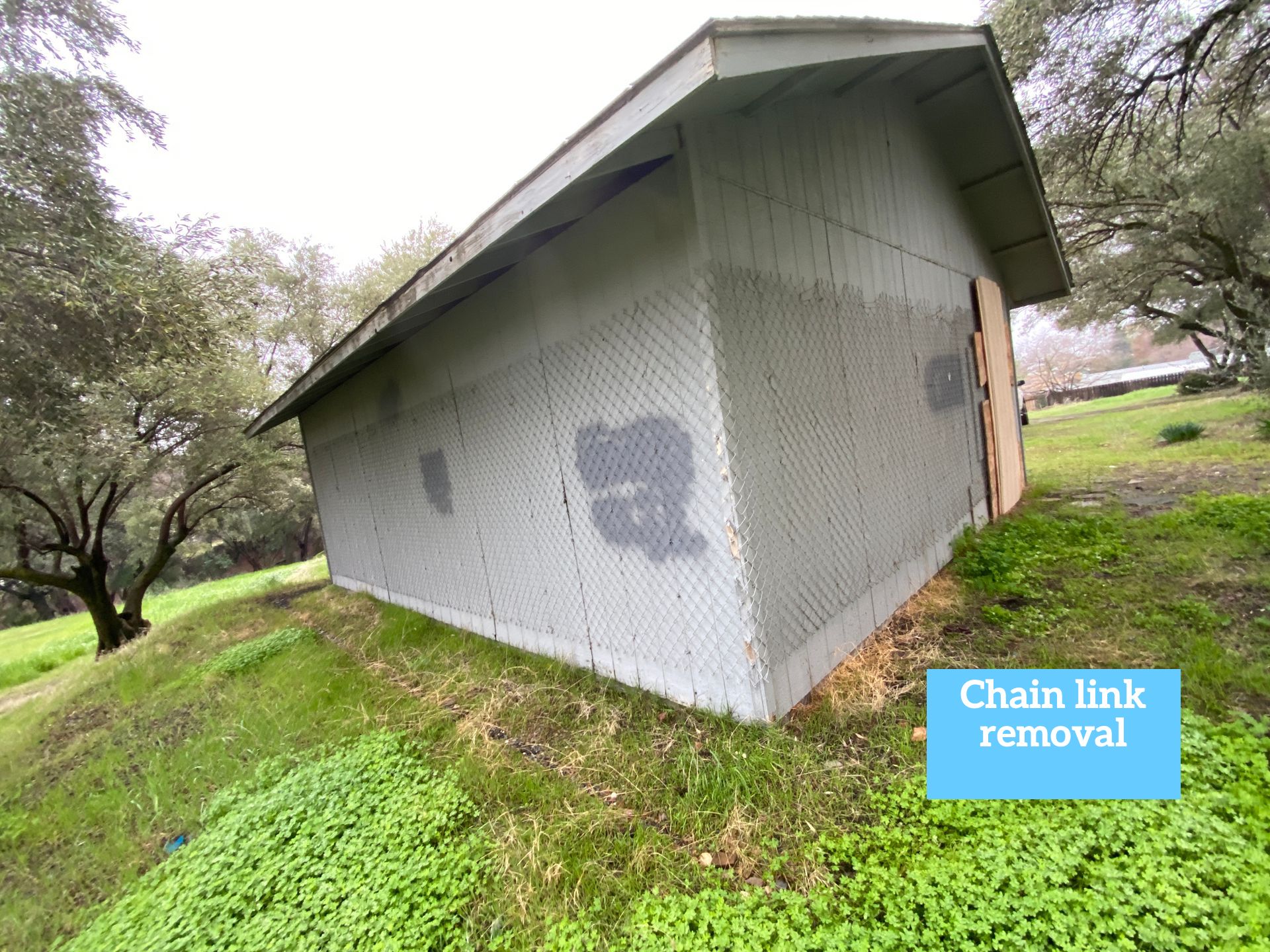 Small gray building on a grassy slope with a chain-link fence removed nearby.