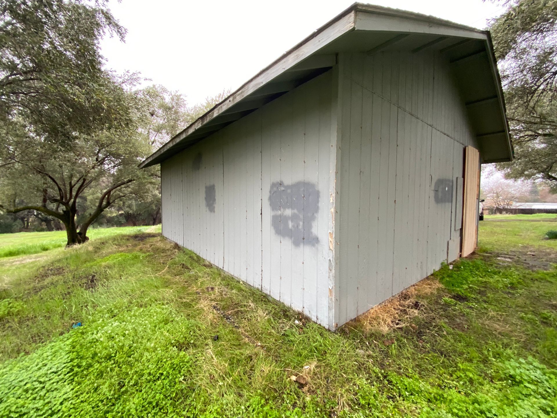 Gray shed with a slanted roof on a grassy hillside, viewed from the corner.