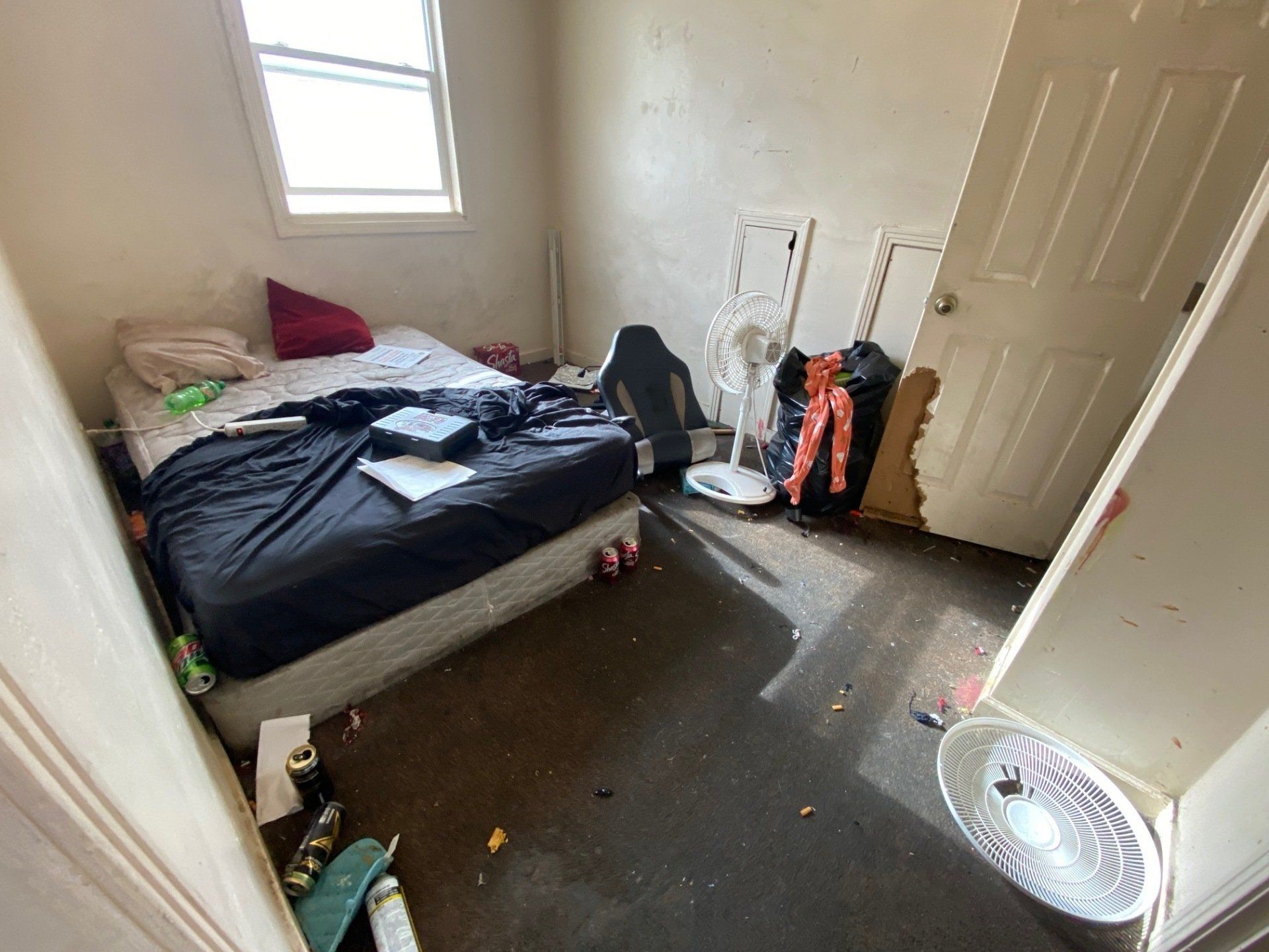 Small cluttered bedroom with unmade bed, window, open closet, and clothes scattered on the floor.