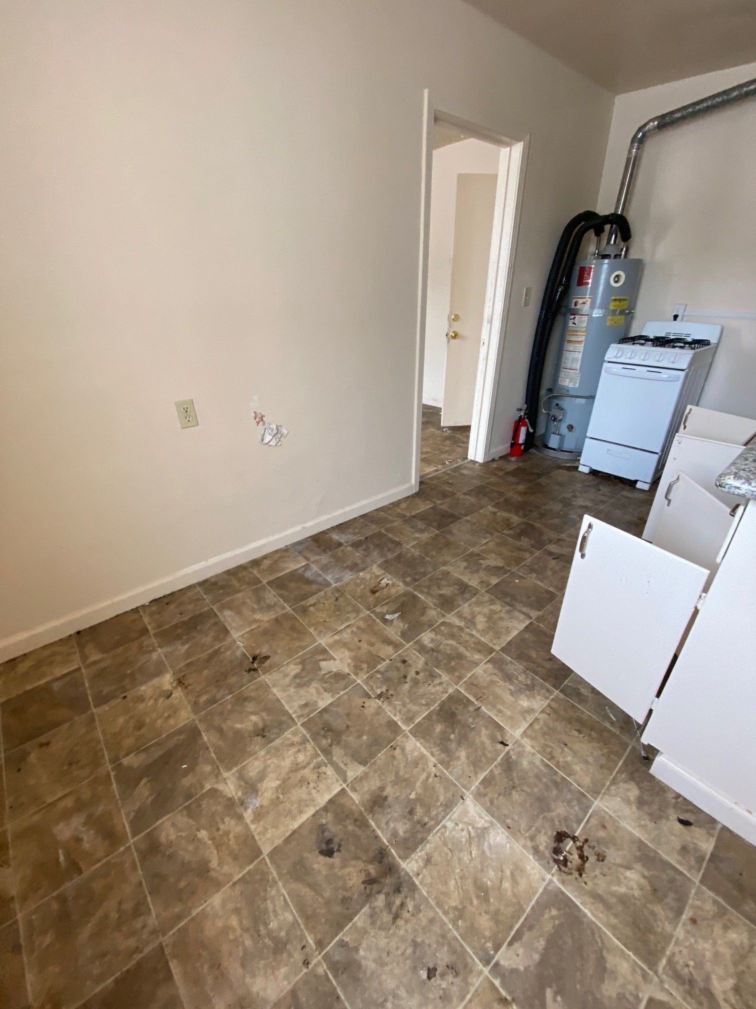 Empty room with brown tile floor, white walls, open door, and laundry appliances in the corner