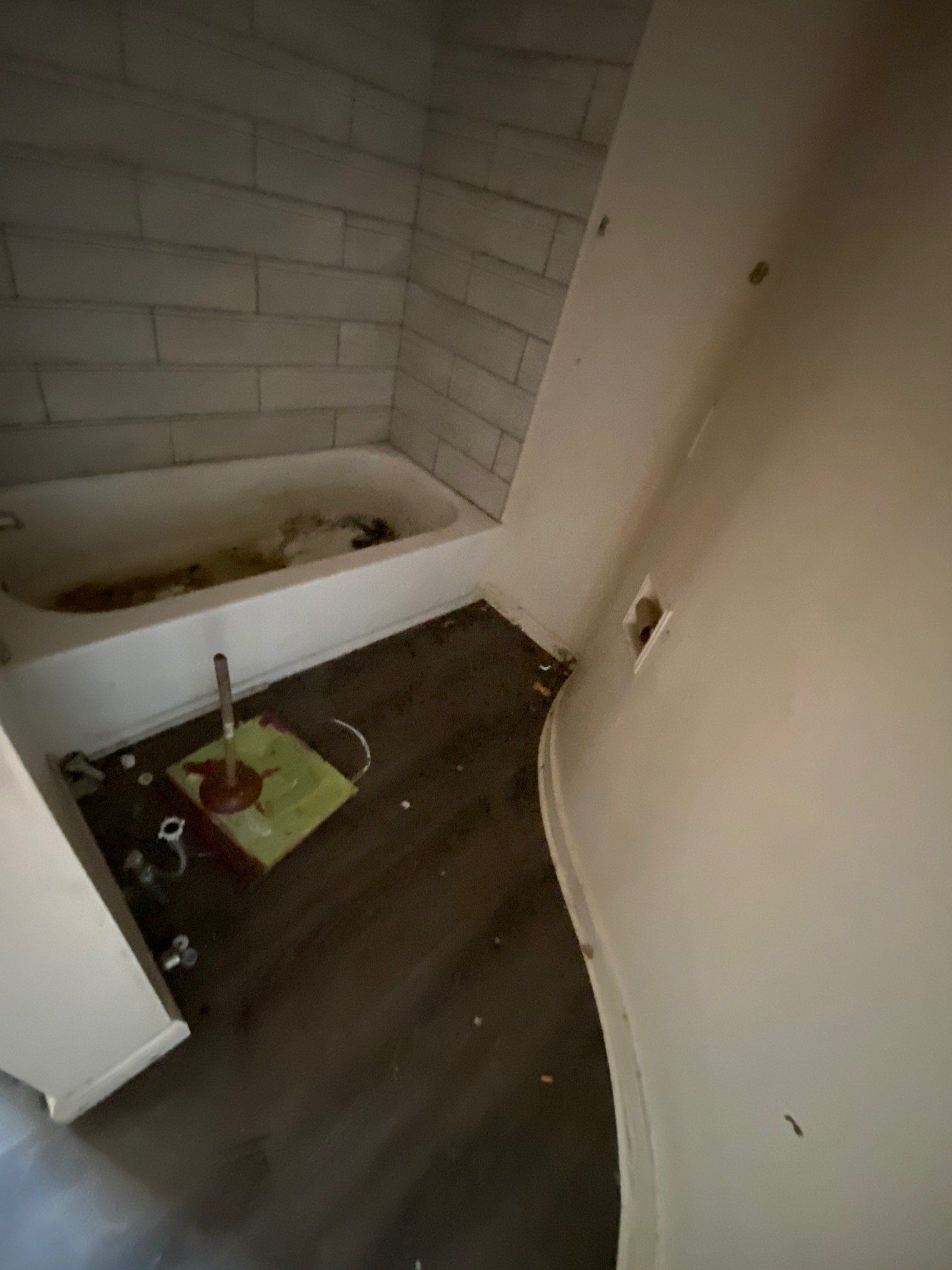 Small bathroom with a toilet, tub, and a green cleaning bucket on dark floor tiles.