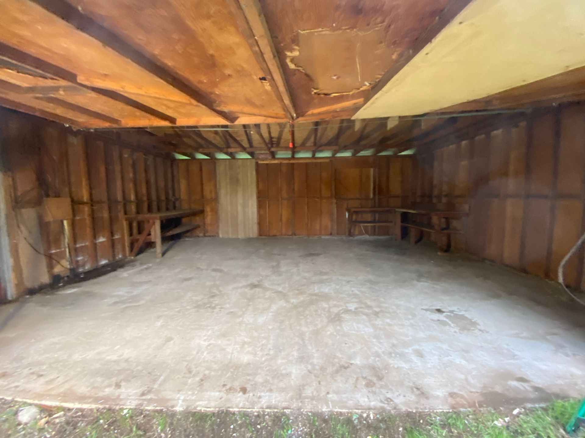 Empty wooden garage interior with concrete floor and workbenches along the back walls