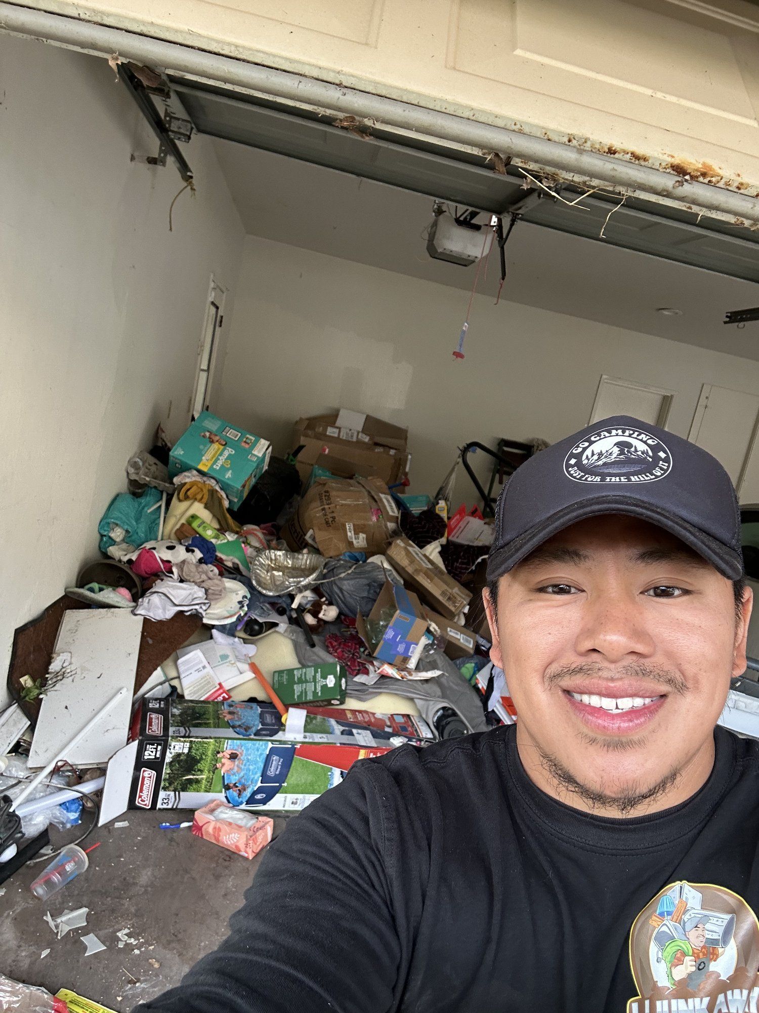 LJ Junk Away crew member smiling in front of a garage full of junk before cleanout