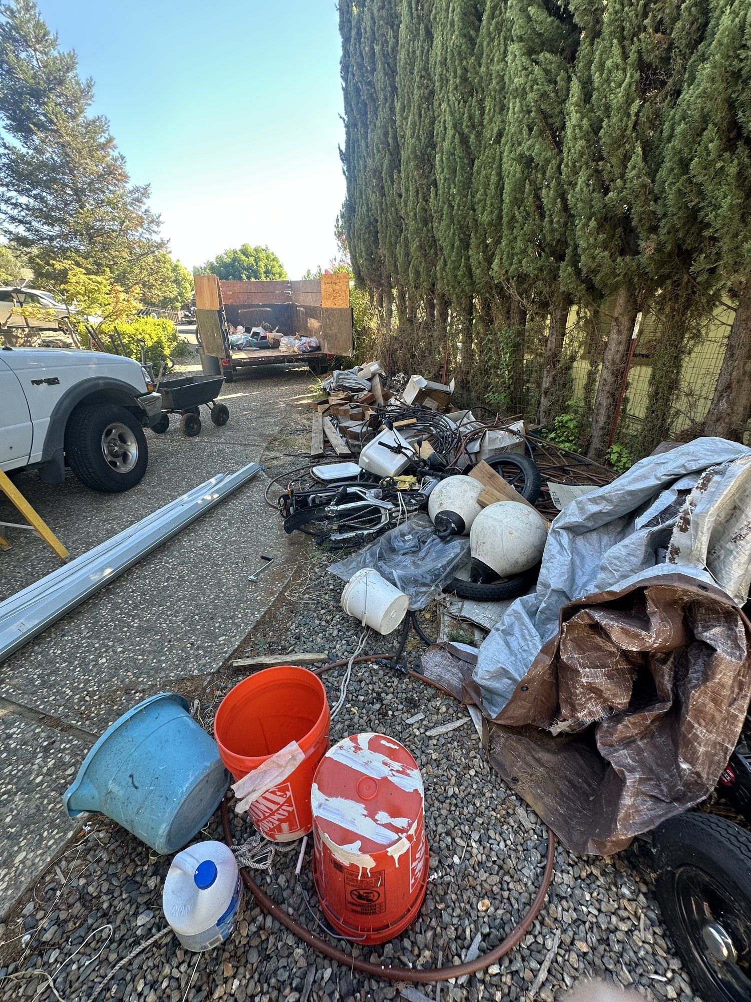 Junk pile with buckets and debris beside a driveway before removal