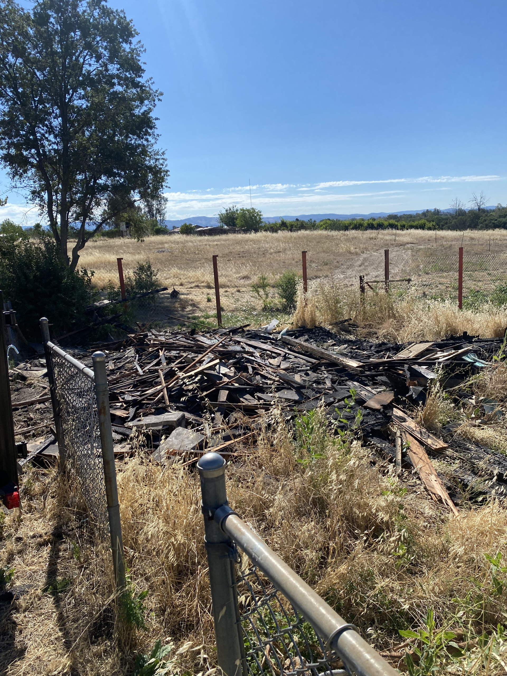 Charred debris in a burned field behind a wire fence under a blue sky