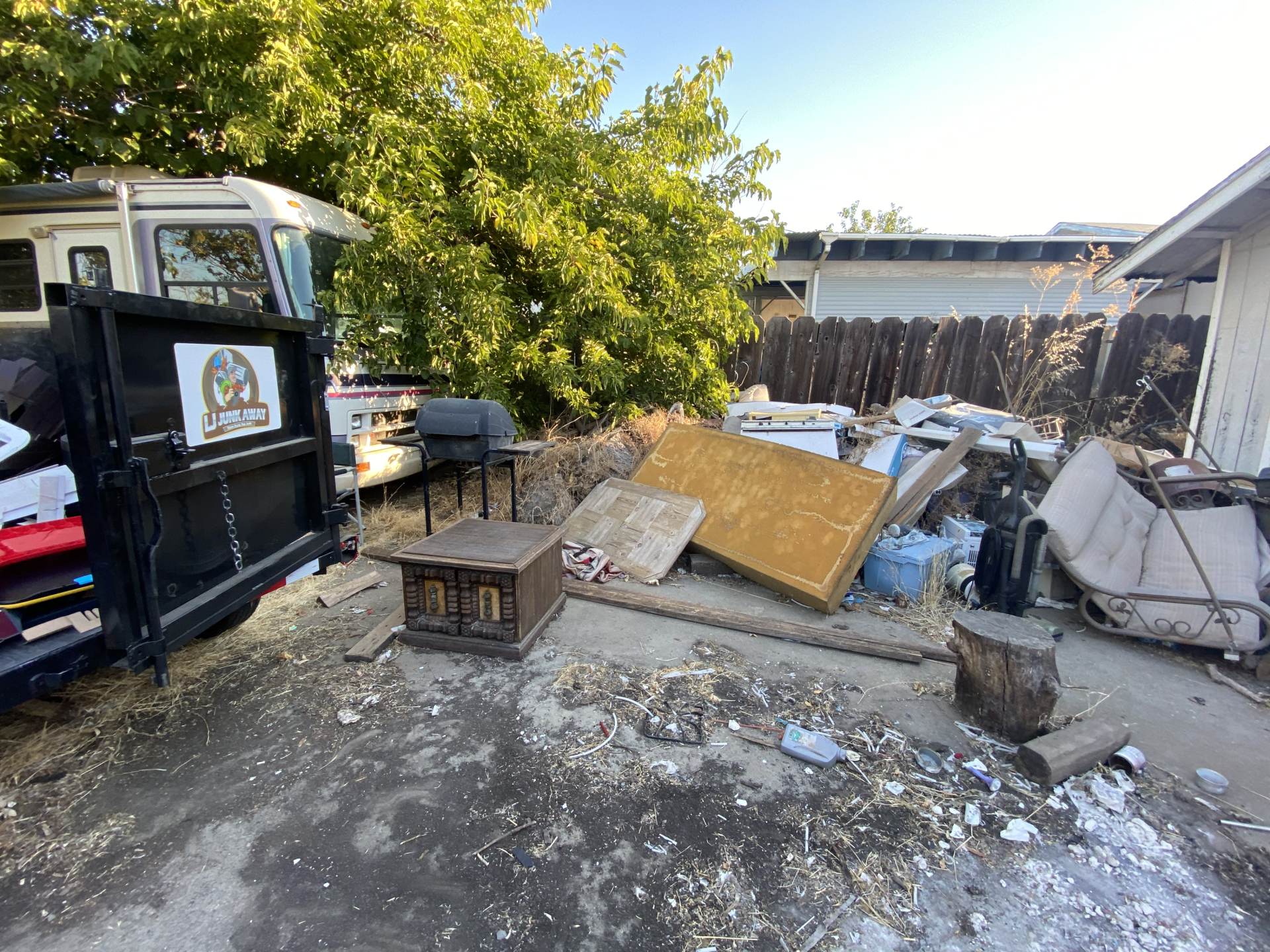 Outdoor cluttered yard with debris, pallets, a barbecue grill, and a truck beside a building