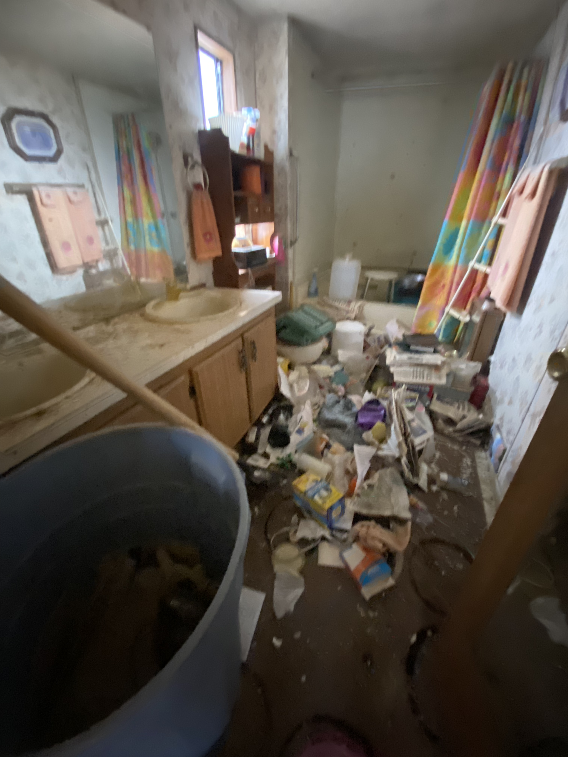 Cluttered, messy room with debris on the floor, a sink cabinet, and colorful items leaning against the wall.