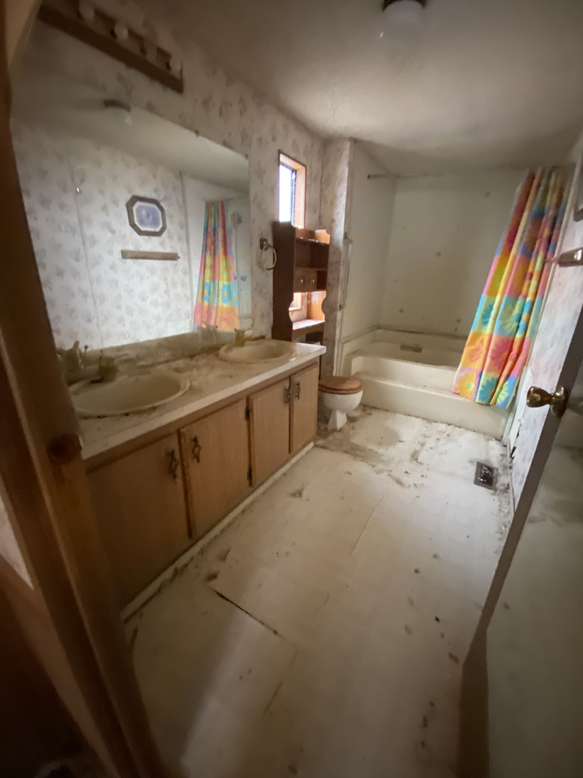 Dingy bathroom with old wood vanity, stained sink, bathtub, and colorful striped shower curtains