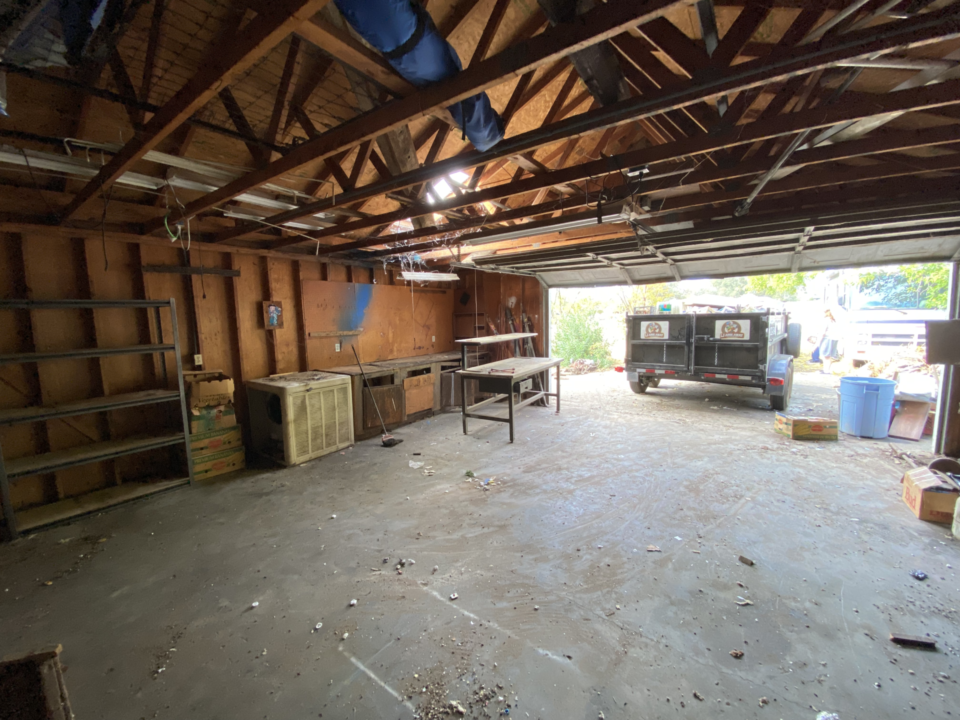 Empty garage with exposed rafters, worktables, and a truck parked near the open doorway.