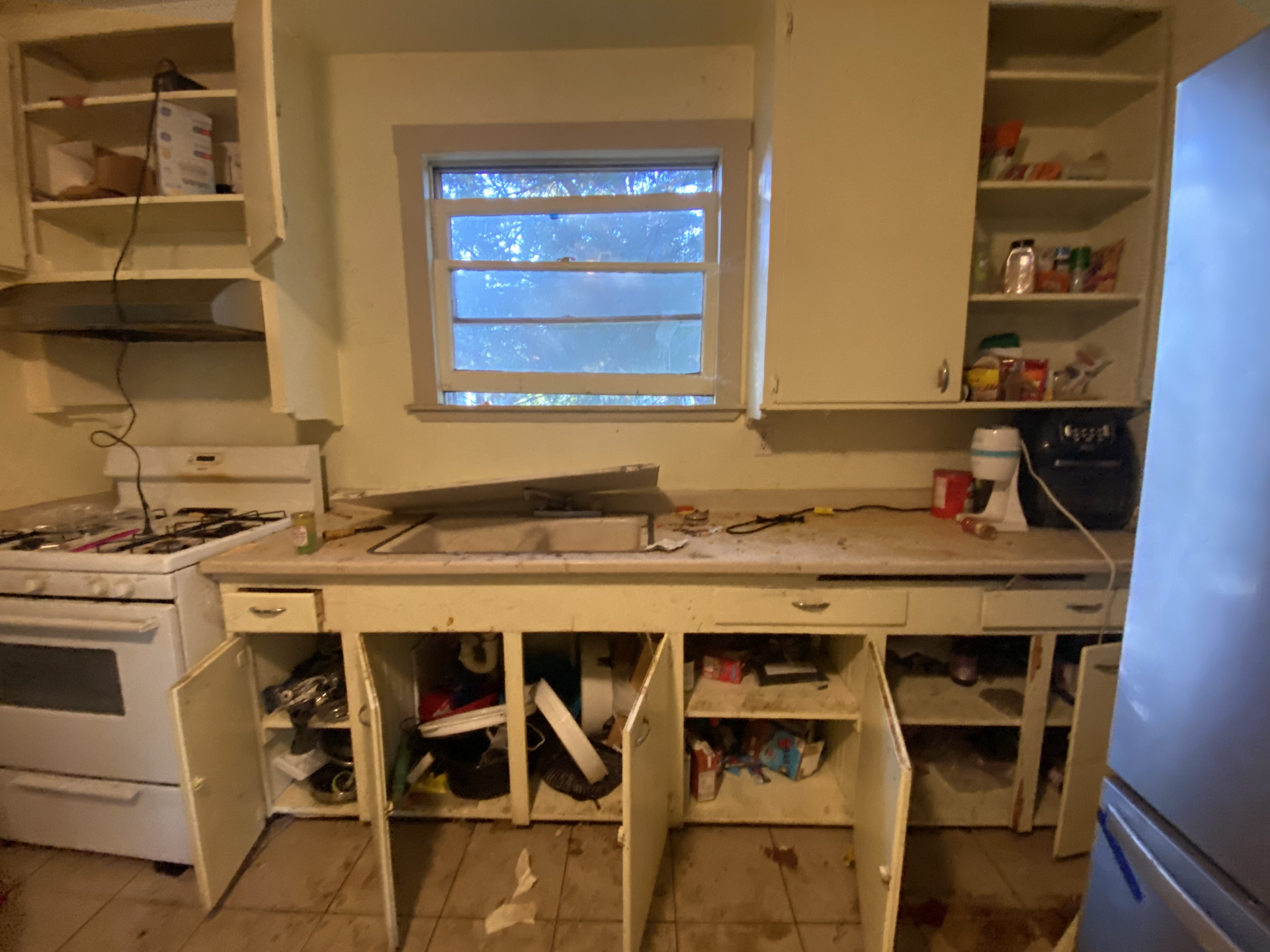 Messy kitchen with open cabinets, cluttered countertops, and a window above the sink.