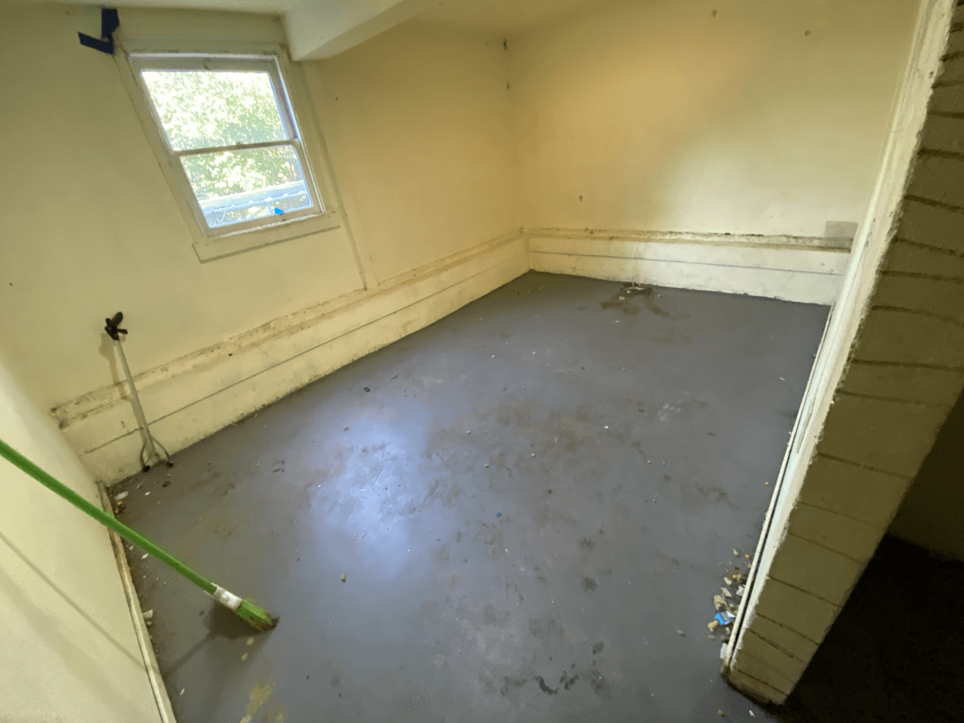 Empty room with bare walls, gray floor, and a window letting in light.
