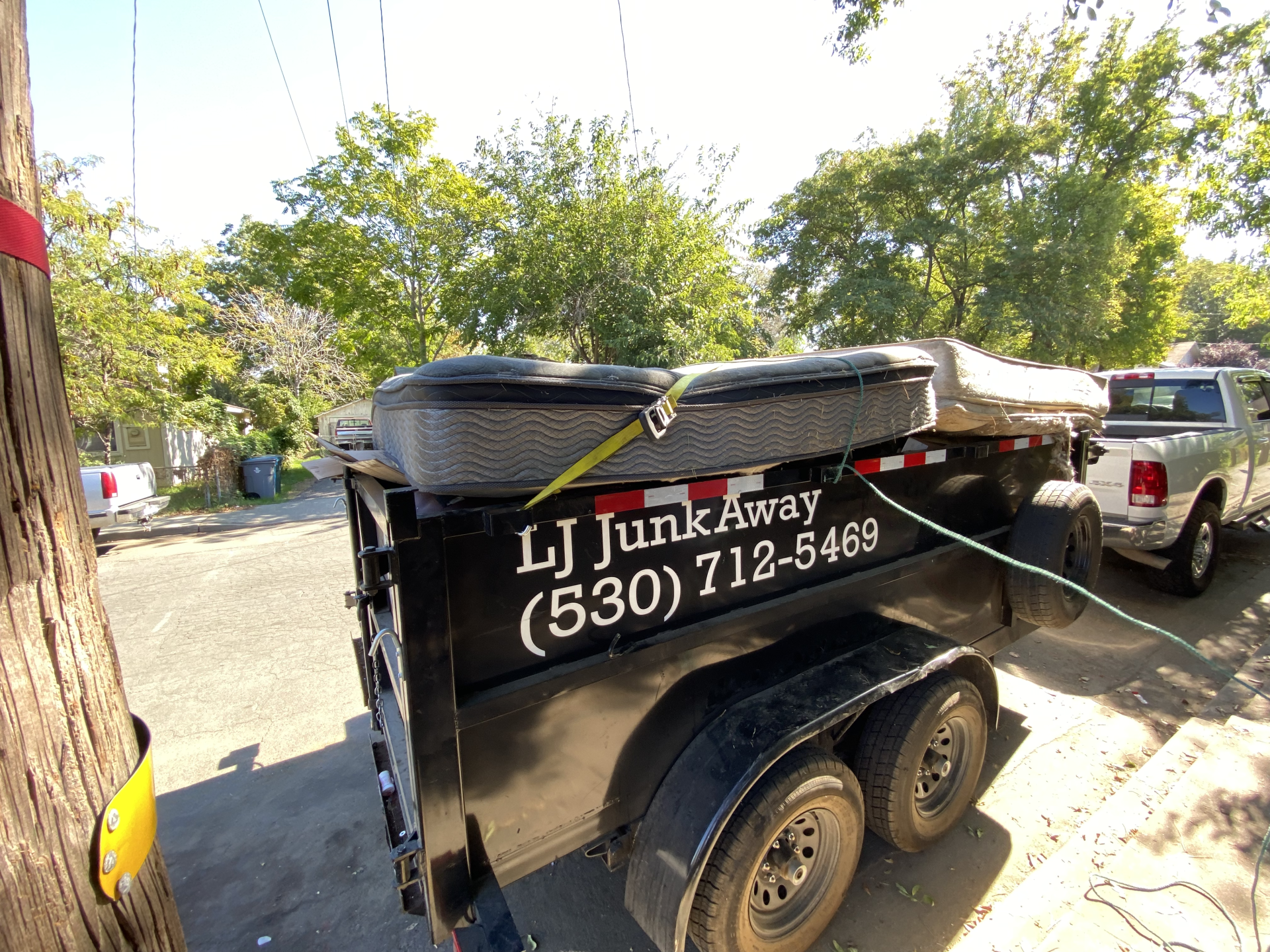 Black junk removal trailer with company phone number parked on a sunny street.