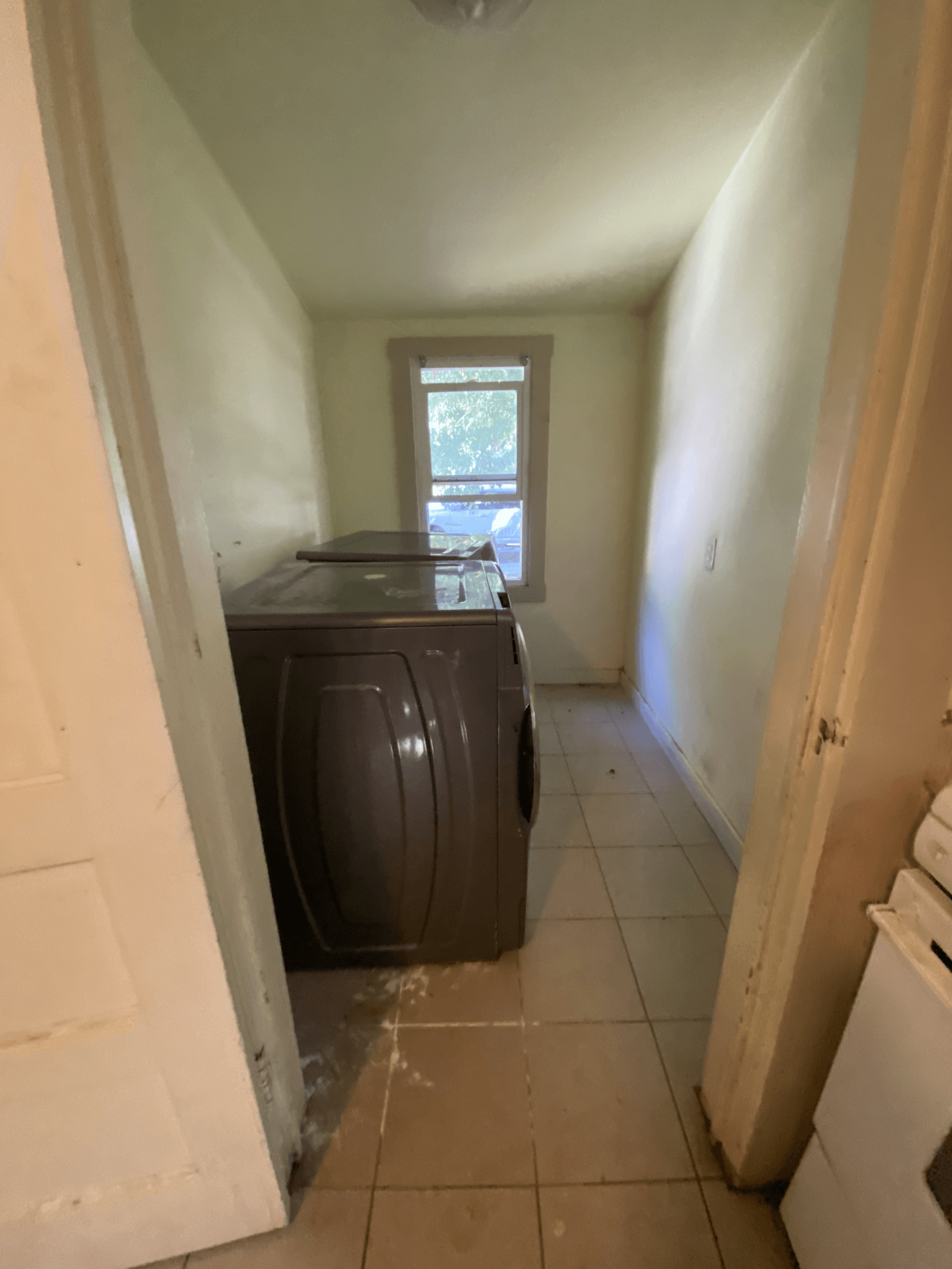 Narrow kitchen hallway with dark cabinets, beige tile floor, and a window at the end.