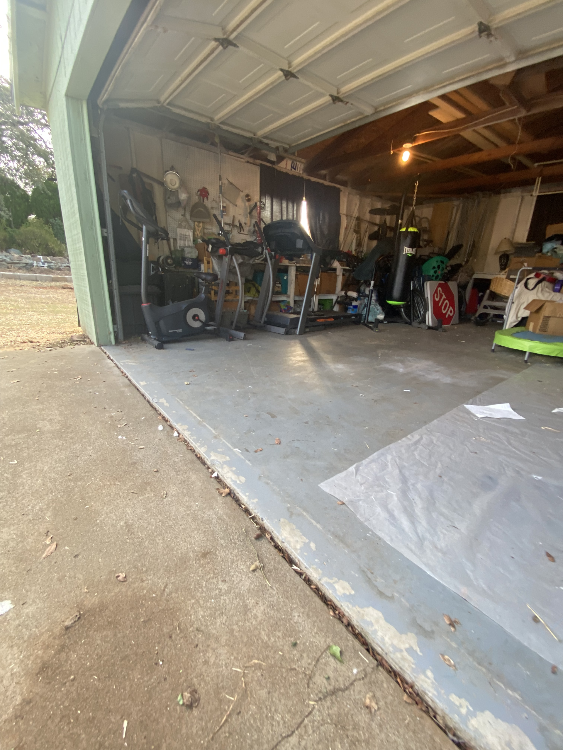 Open garage with tools, equipment, and a concrete floor, viewed from the driveway.