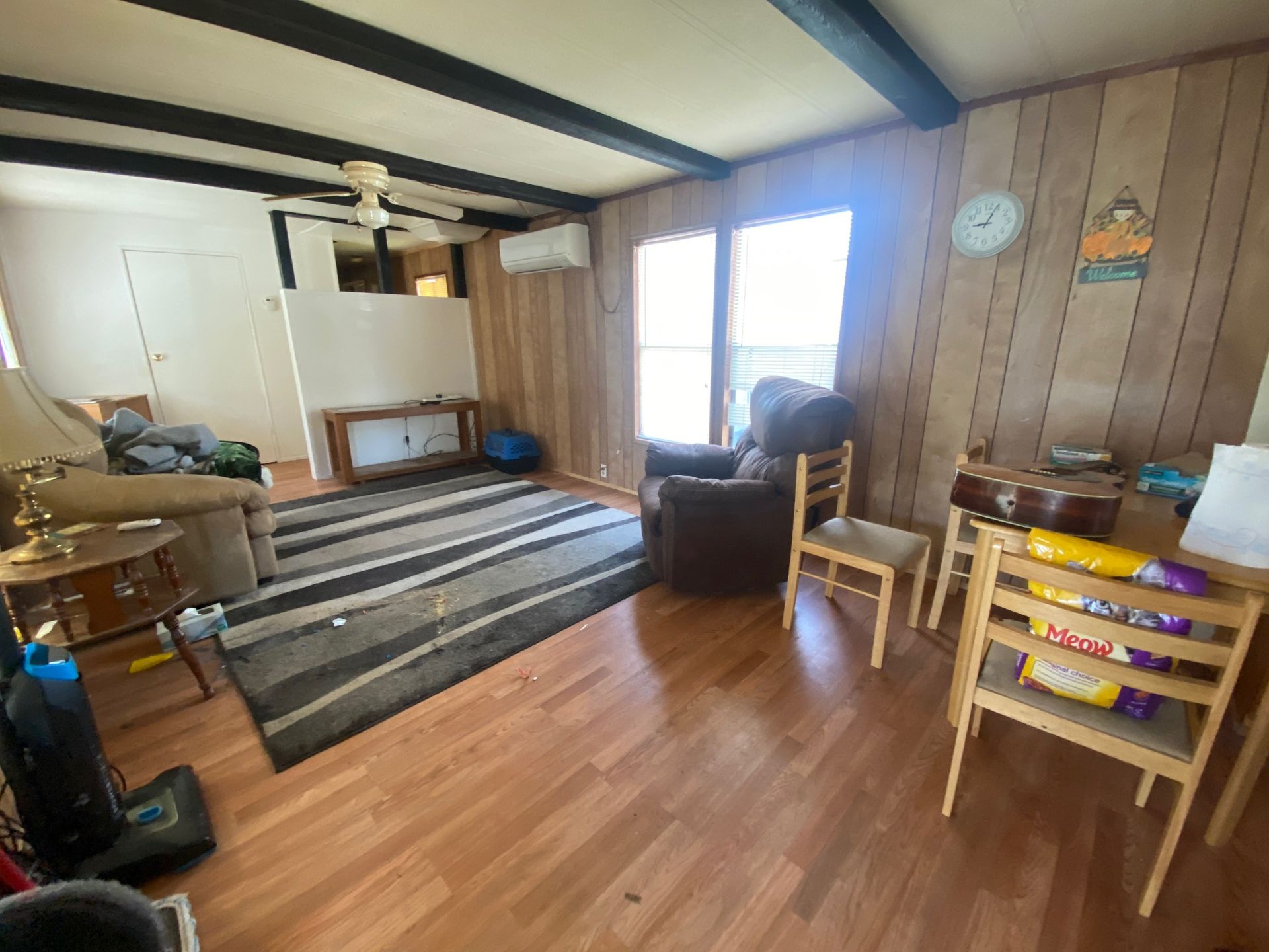 Cozy living room with striped rug, chairs, wooden table, TV stand, and sunlight through window blinds