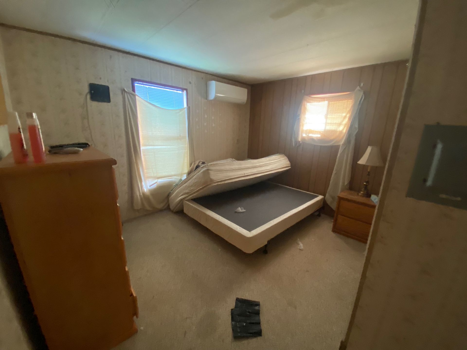 Small bedroom with a bed, dresser, windows with blinds, and a pile of clothes on the floor.