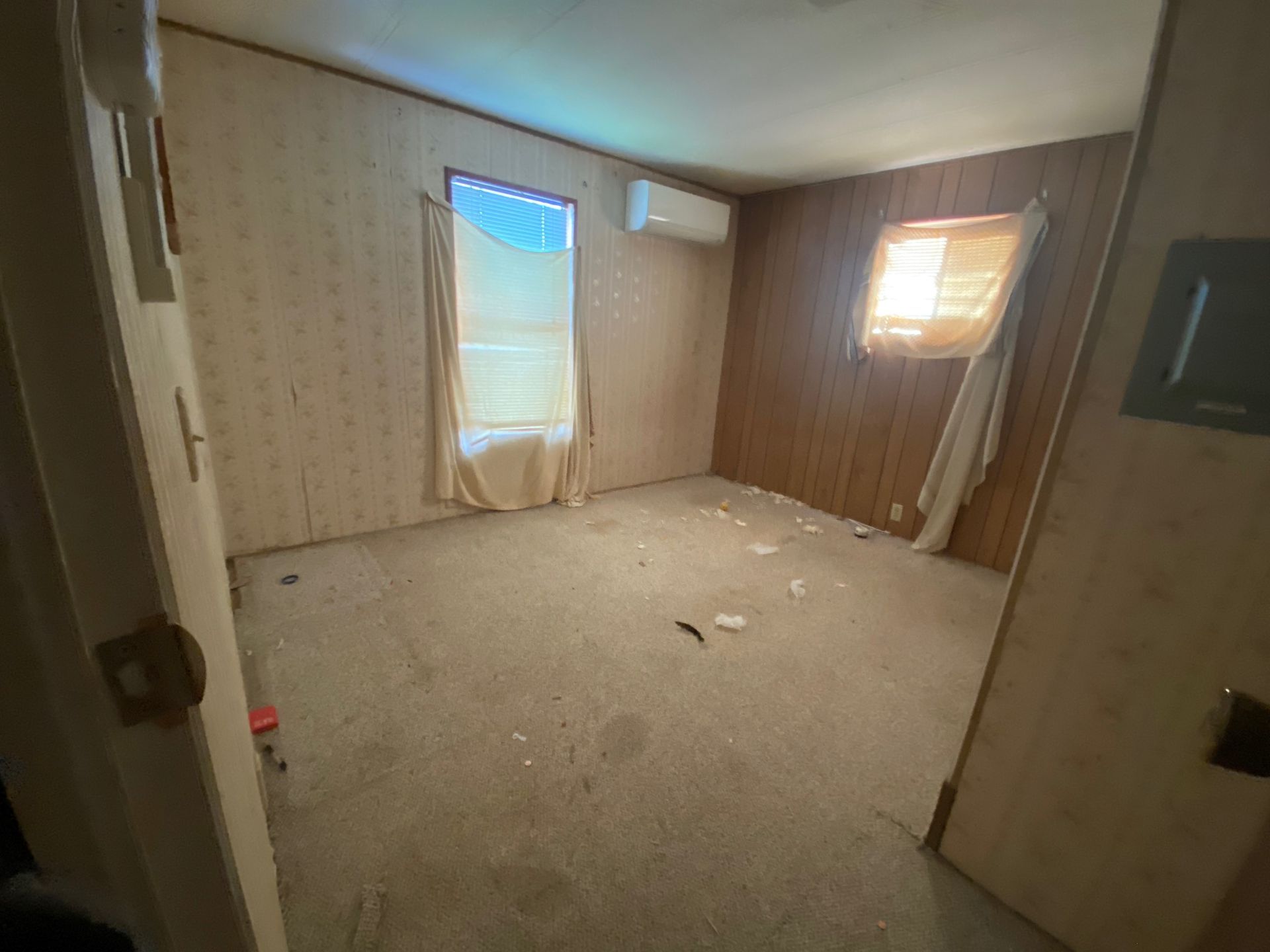 Empty beige room with carpet, two windows with curtains, and a wall-mounted TV frame