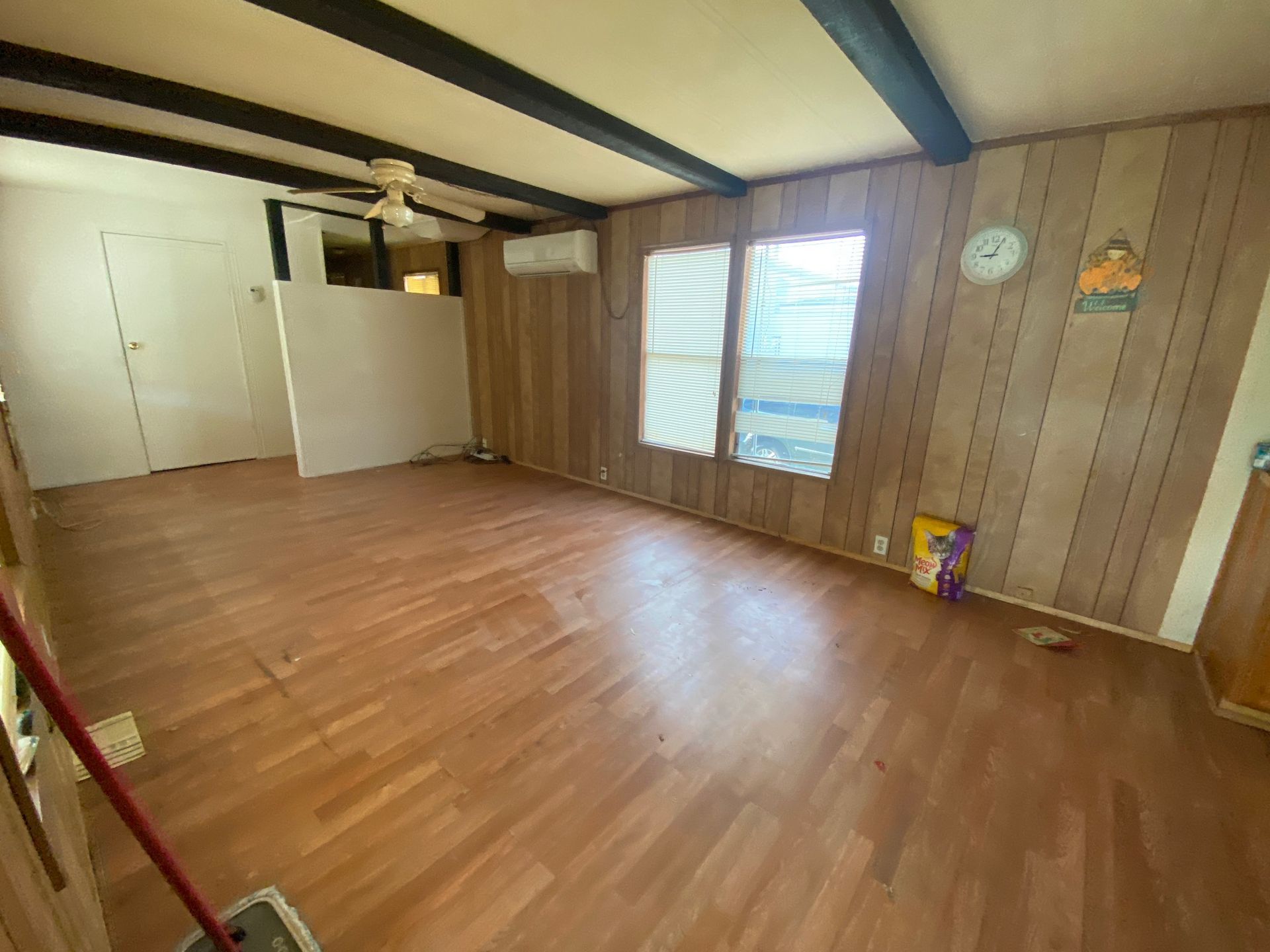 Empty wood-floored room with brown paneled walls, white closet doors, and a window with blinds.