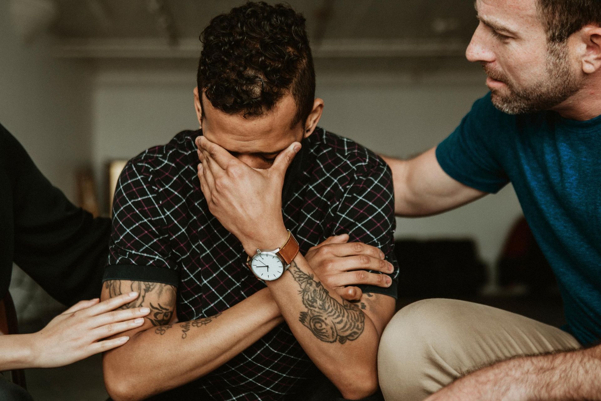 Man with head in hands, comforted by people placing hands on his shoulders.