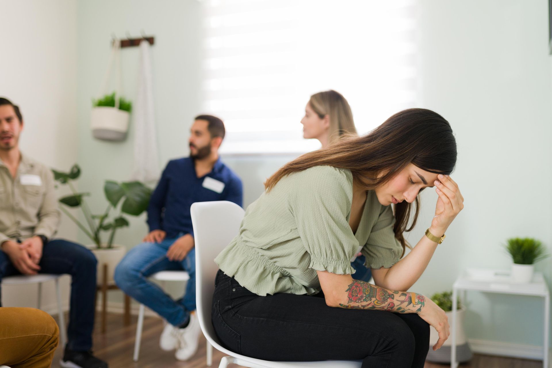 Woman with head in hand in group therapy session. Others seated, looking on.