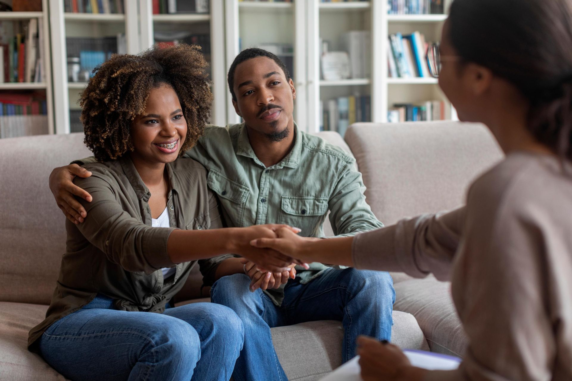 Couple shaking hands with a therapist on a couch in an office, bookshelves in the background.