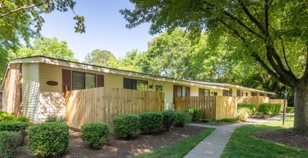 Row of tan townhouses with brown doors, wooden fences, and green landscaping.