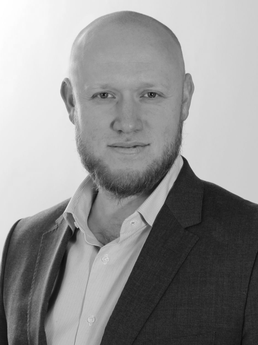 Plešatý muž v obleku, dívající se do kamery, s lehkým úsměvem.